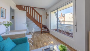 A modern apartment with a wooden staircase, a dining area with outdoor seating, and large windows offering a view of the city. - Duplex Les Mouettes - Welkeys (Cabourg)