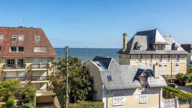 A coastal residential area with a mix of modern and traditional architecture, including a house with a sloped roof and a balcony, and a building with a flat roof and a chimney. - Duplex Les Mouettes - Welkeys (Cabourg)