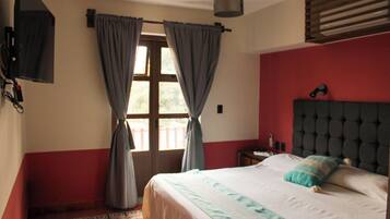 Un dormitorio con cama, cortinas, mesita de noche, lámpara y ventana con persianas.