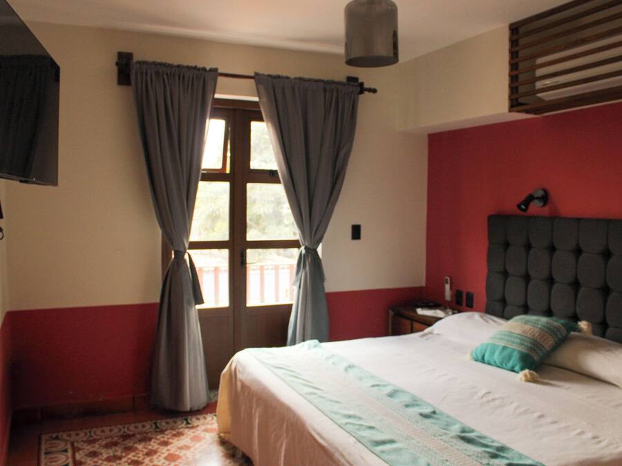 Un dormitorio con cama, cortinas, mesita de noche, lámpara y ventana con persianas.