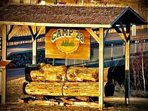 A wooden structure labeled "Camp 26" with a rustic design, featuring a log bench and a small shelter.