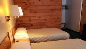 Une chambre avec deux lits, des murs lambrissés et une lampe fixée au mur, ainsi qu'un porte-manteau.