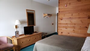 Une chambre à coucher comprenant un lit, une commode, une chaise, un téléviseur et un mur en bois.