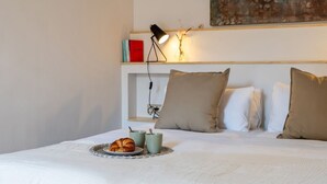 A neatly made bed with a plate of croissants and two mugs, a bedside lamp, and a shelf with books and a decorative item. - Beautiful apartment near Plaza Catalunya (Barcelona)