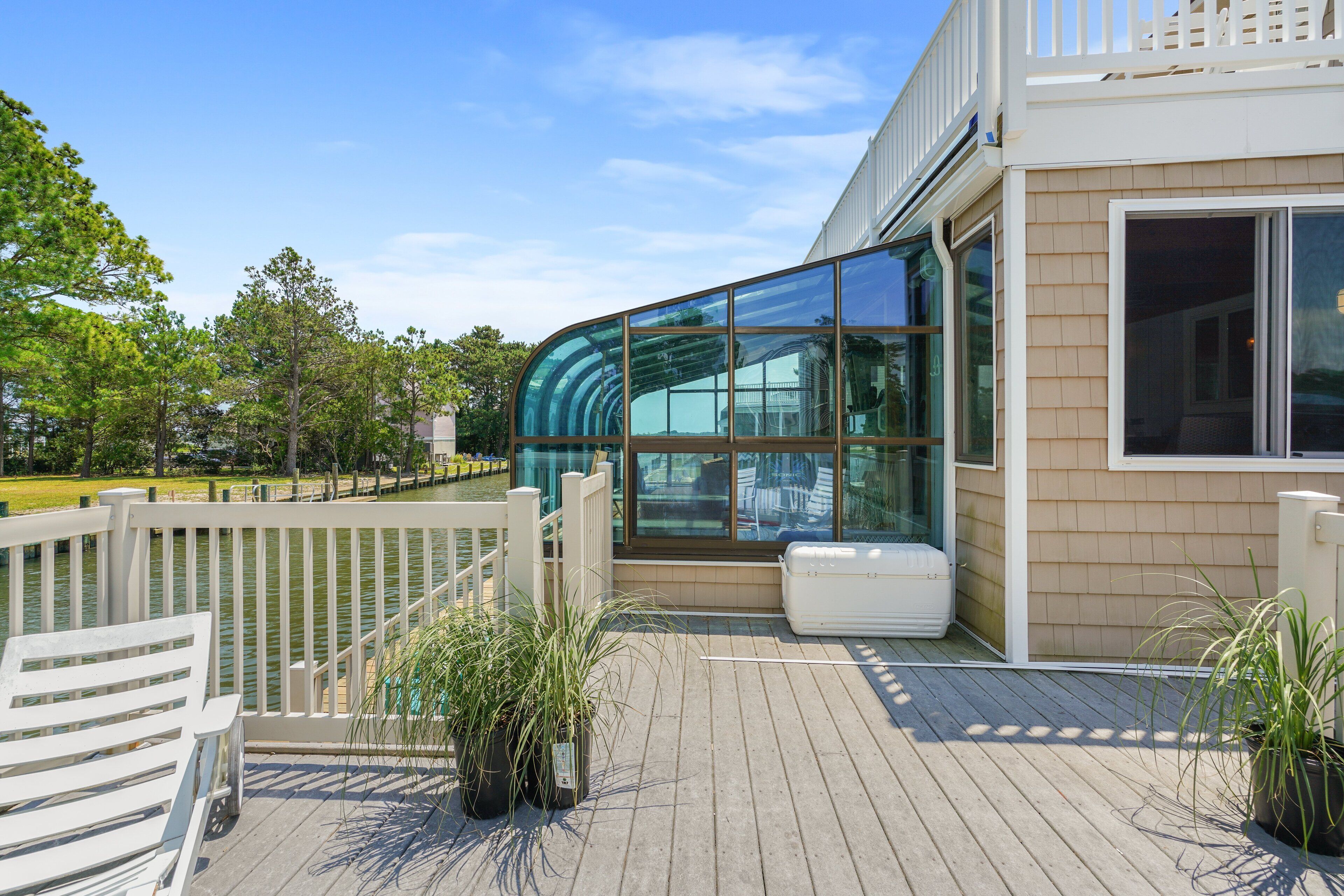 A modern building with large glass windows, a wooden deck, and a white fence.