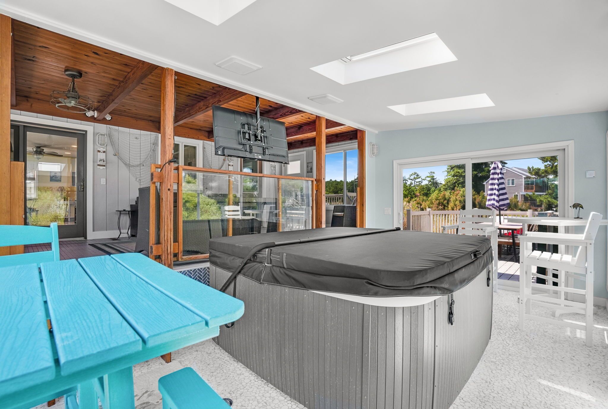A modern outdoor living area with a hot tub, wooden ceiling, and glass doors leading to a patio.