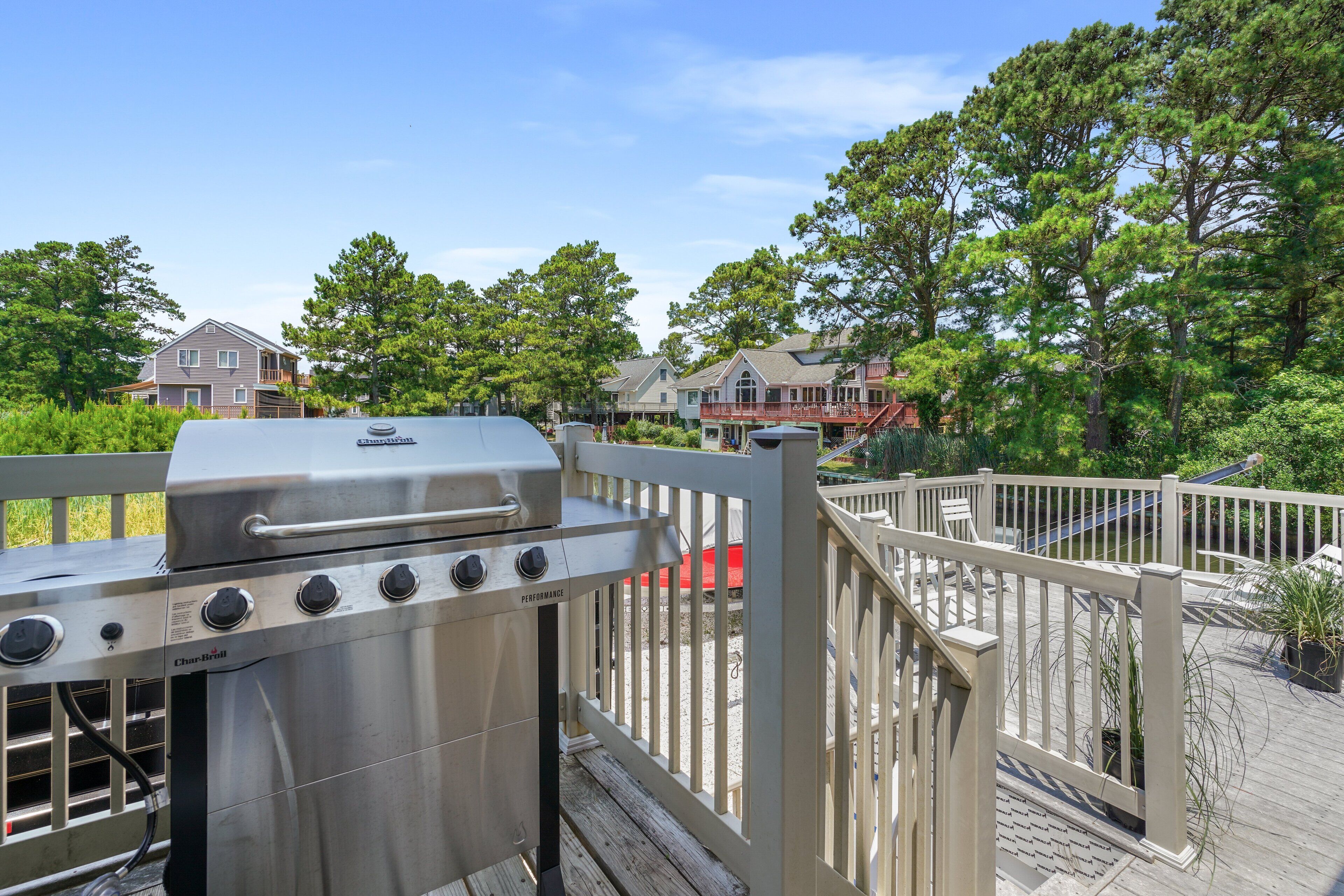 Un barbecue installé sur une terrasse en bois, avec en arrière-plan des maisons et des arbres.