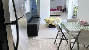 Kompakti oleskelutila, jossa on pieni keittiö, ruokailualue, sohva ja taustalla sänky.