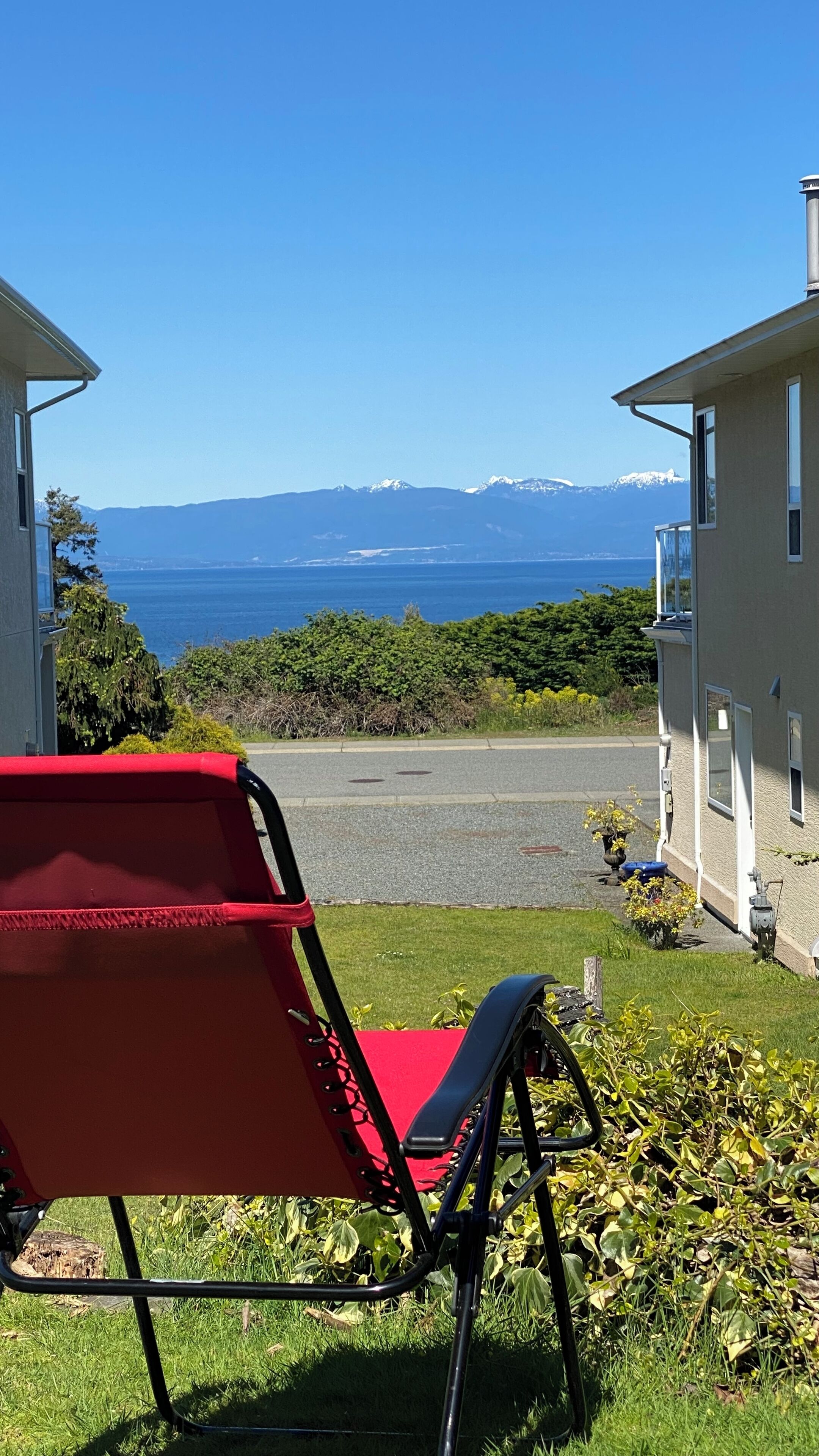 Un fauteuil rouge est placé sur une pelouse verdoyante, offrant une vue sur une montagne et la mer.