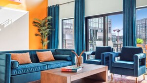 A modern living room with a blue sofa, matching armchairs, and a wooden coffee table. A large window offers a view of the cityscape. - Tequila Sunrise Downtown Condo, Walk to Broadway! (Nashville)