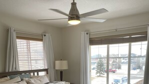 Une chambre à coucher avec un lit, un ventilateur de plafond, une fenêtre avec des rideaux et une vue sur l’extérieur.