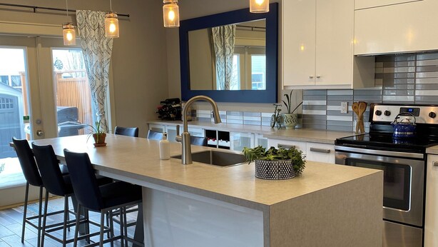 Une cuisine moderne dotée d’un îlot central, d’appareils électroménagers en acier inoxydable, de luminaires suspendus et d’une grande fenêtre.