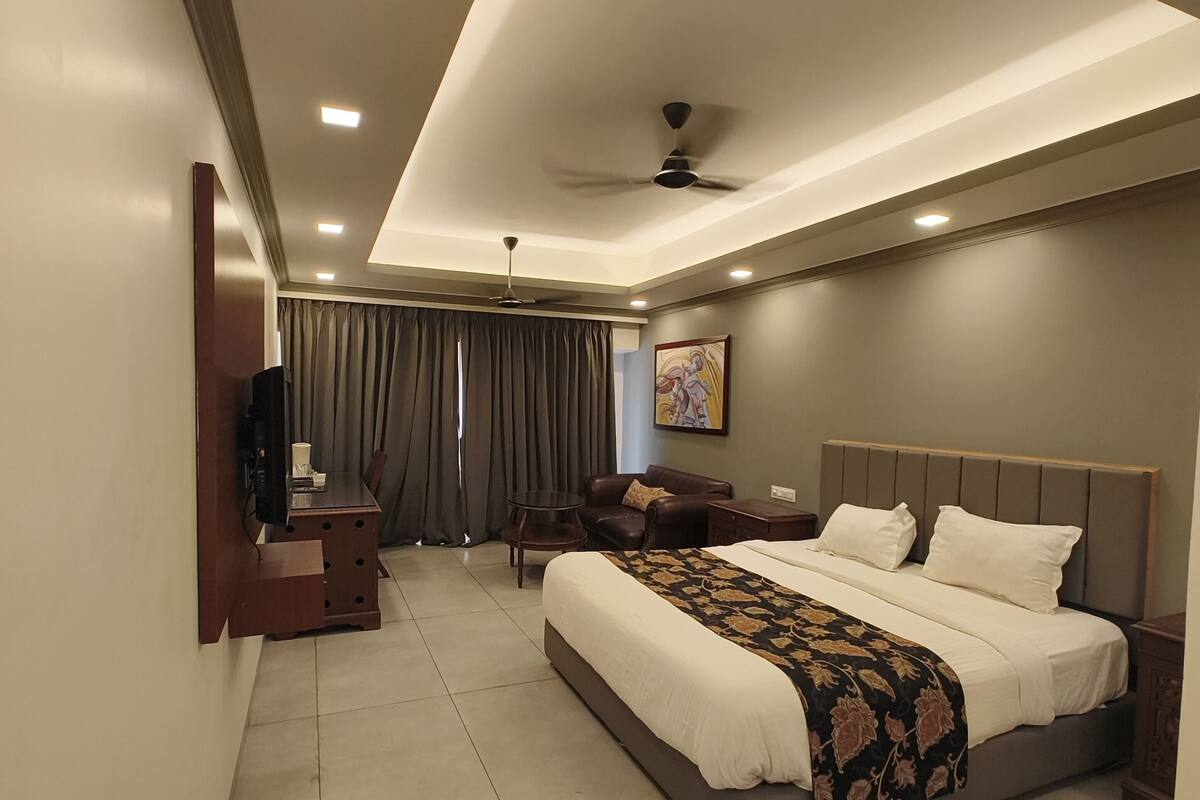 Une chambre moderne avec un grand lit, un téléviseur fixé au mur, un ventilateur de plafond et un bureau avec une chaise.