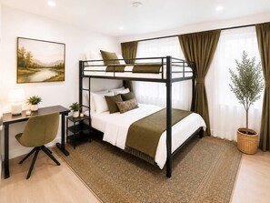 Una cama individual superpuesta con escritorio y silla, una planta en maceta y un cuadro en la pared.