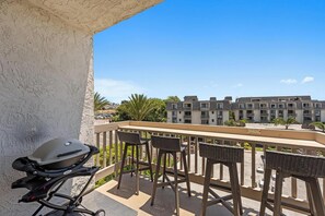 A balcony with a grill, wicker chairs, and a view of a multi-story building.