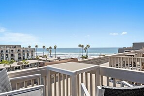 A beachfront property with a view of the ocean, palm trees, and a building with balconies.