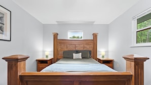 A bedroom with a wooden bed, two bedside tables, a nightstand, a window with a view of trees, and a framed picture on the wall. - Lake Cabin, 10 minutes from Callaway Gardens  (West Point)