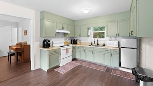 A kitchen with light green cabinets, a white stove, and a microwave. There is a wooden table and chairs in the adjacent dining area. - Lake Cabin, 10 minutes from Callaway Gardens  (West Point)