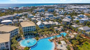 A resort with a large central pool, multiple buildings, and a view of the ocean.