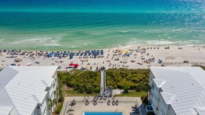 An aerial view of a beach with numerous umbrellas and sun loungers, a lifeguard tower, and a pool area in the foreground.