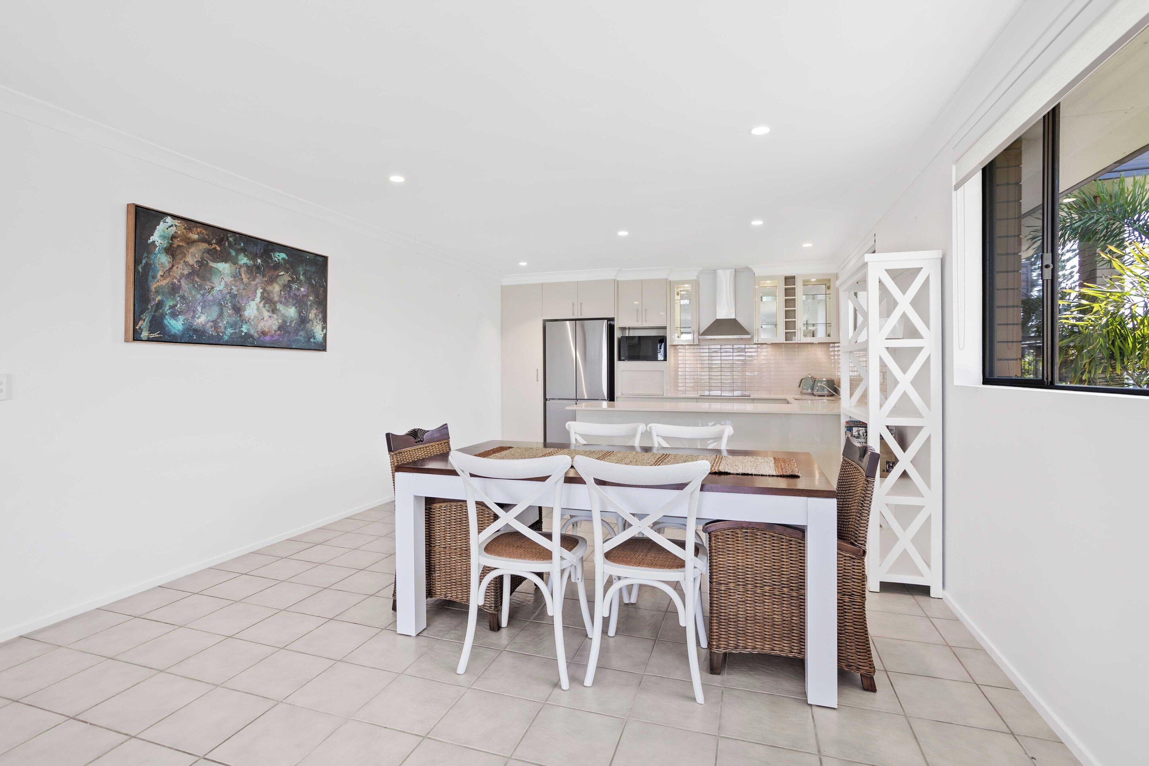Een moderne keuken met witte kasten, een roestvrijstalen koelkast en een eethoek met een houten tafel en witte stoelen.