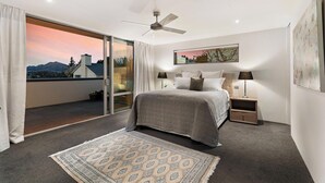 A bedroom with a bed, two bedside tables, a ceiling fan, a large window with a view of mountains, and a painting on the wall. - Lake & Mountain views, close to ski fields. Executive living - 3 bed/3 bath, spa (Wānaka)
