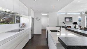 A modern kitchen with white cabinetry, a stainless steel refrigerator, a built-in oven, and a large island with a granite countertop. - Lake & Mountain views, close to ski fields. Executive living - 3 bed/3 bath, spa (Wānaka)