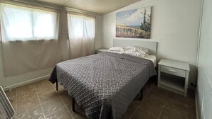 Ein Schlafzimmer mit Bett, Nachttisch, Fenster mit Vorhängen und einem Bild an der Wand.