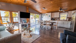 A spacious living area with a wooden ceiling, a dining table, and a kitchen with white cabinets. - Pelicans View - Venture Out Lot 318 (Cudjoe Key)