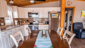 A spacious kitchen with wooden cabinets, a central island, and a dining area with a long table and chairs. - Pelicans View - Venture Out Lot 318 (Cudjoe Key)