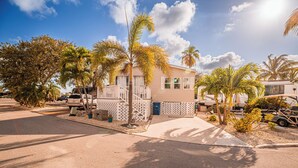 A single-story house with a white porch, surrounded by palm trees and a clear sky. - Pelicans View - Venture Out Lot 318 (Cudjoe Key)