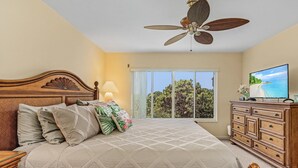 Una camera da letto con un letto, una ventola a soffitto, una cassettiera, una televisione e una finestra vista alberi.