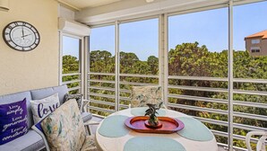 Un balcone con vista sul verde, un tavolo rotondo con un oggetto decorativo e una sveglia appesa al muro.