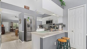 Une cuisine moderne avec des meubles blancs, des appareils en acier inoxydable et un îlot central doté de tabourets.