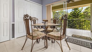 Un coin repas avec une table ronde et des chaises en osier, une porte blanche et un balcon donnant sur la forêt.
