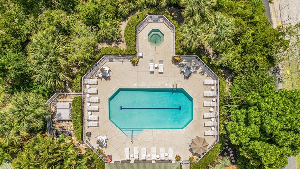 Vue aérienne d’un complexe hôtelier doté d’une piscine centrale, entourée de chaises longues et d’un espace de détente abrité.