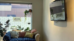 A modern living room with a sofa, a TV mounted on the wall, and a window with plants.