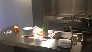 A modern kitchen with a stainless steel countertop, a built-in stove, and a sink. There is a bar stool, a candle, and a green bottle on the counter.