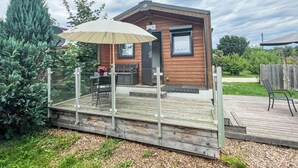 Eine kleine Holzhütte mit einer Terrasse, einem Tisch und Stühlen, und einem großen Sonnenschirm, der Schatten spendet.