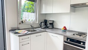 Eine moderne Küche mit weißen Schränken, einer Edelstahl-Spüle, einer Kaffeemaschine und einem Backofen.