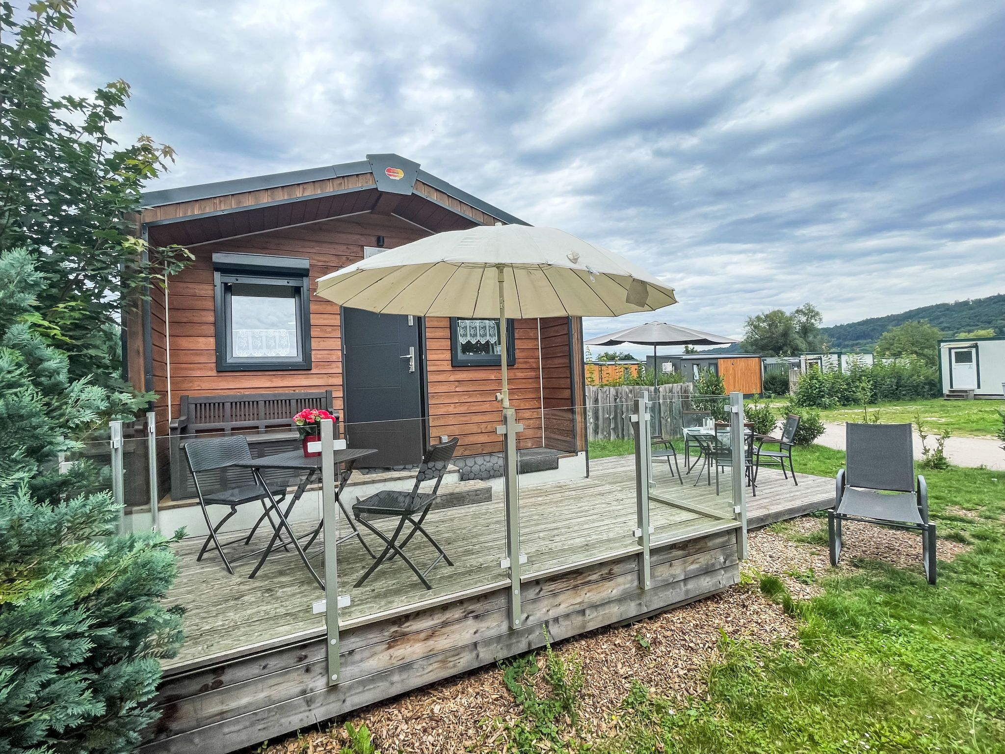 En træhytte med terrasse, udendørs møbler og en stor parasol.