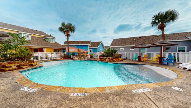 A swimming pool with a 4 FT 6 IN depth marker, surrounded by houses with a white picket fence, and a no diving sign on the poolside. - PB205 Shared Pool. Pet Friendly, Parking for 2 Vehicles (Port Aransas)