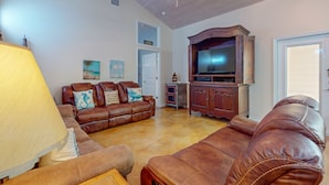 A living room with a brown leather sofa, a wooden cabinet, and a ceiling fan. - PB205 Shared Pool. Pet Friendly, Parking for 2 Vehicles (Port Aransas)