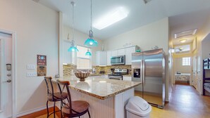 A modern kitchen with white cabinets, a granite countertop, stainless steel appliances, and pendant lighting. - PB205 Shared Pool. Pet Friendly, Parking for 2 Vehicles (Port Aransas)