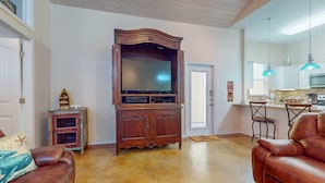 A living room with a large wooden entertainment center, a brown leather sofa, and a kitchen area with a dining table and chairs. - PB205 Shared Pool. Pet Friendly, Parking for 2 Vehicles (Port Aransas)