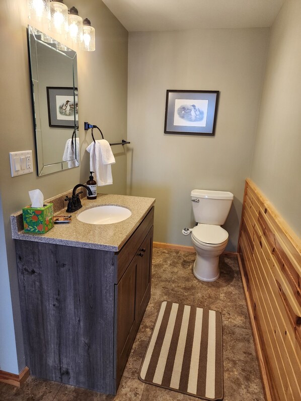 A bathroom with a wooden vanity, a sink, a mirror, a toilet, and a shower area.