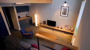 Un salon moderne comprenant un canapé, une table basse, un téléviseur et un coin cuisine avec des placards et un évier.