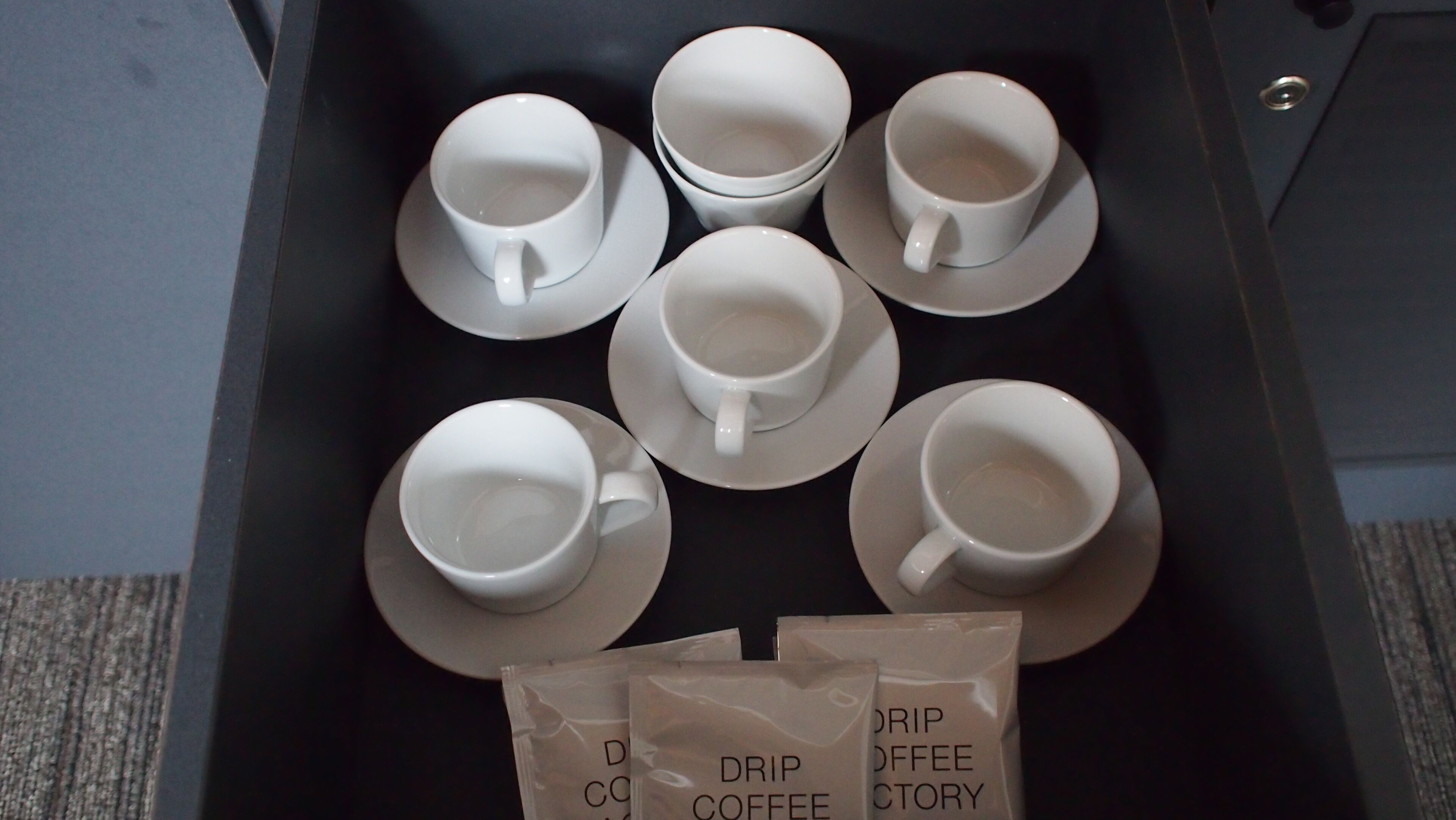 A tray with six white cups and saucers and two drip coffee packets.