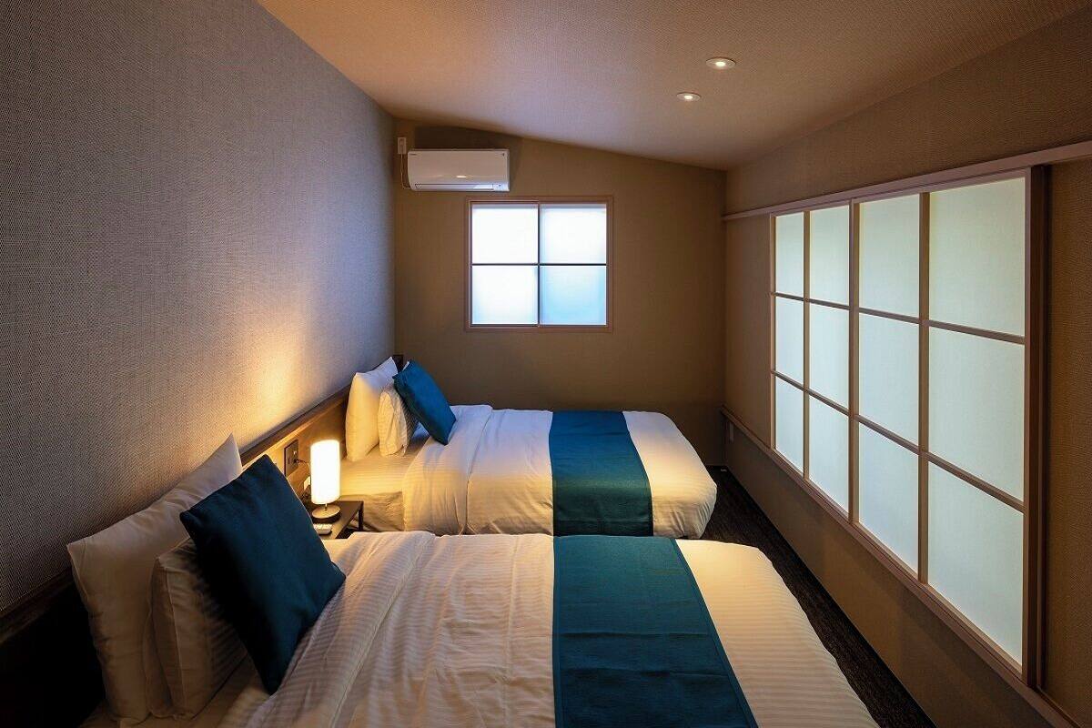 A hotel room with two beds, a window with frosted glass, and an air conditioning unit.
