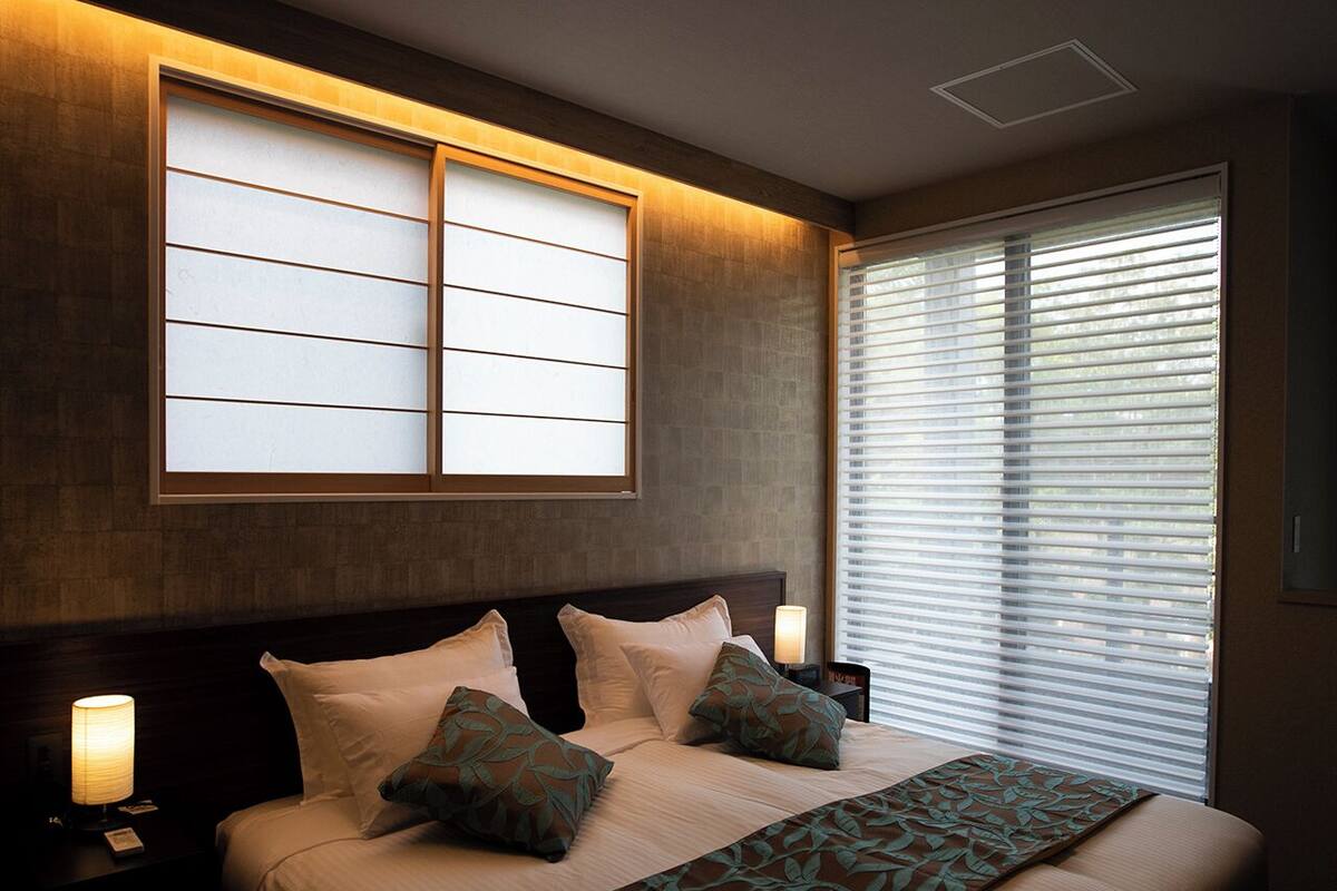 A hotel room with a large bed, bedside lamps, a window with blinds, and a ceiling light fixture.
